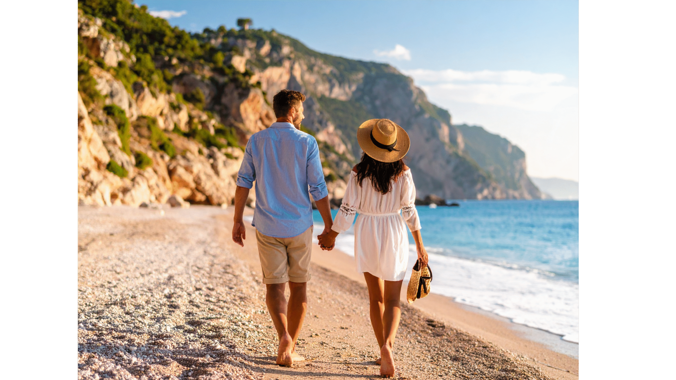 Para trzymająca się za ręce spaceruje boso po kamienistej plaży, w tle morze i skaliste klify.