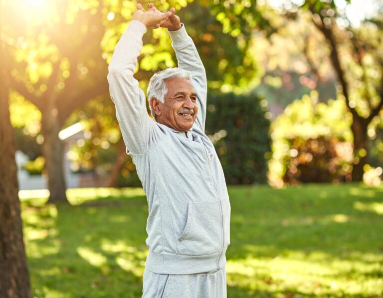 Starszy mężczyzna w sportowym dresie wykonujący poranne rozciąganie w parku, w promieniach słońca.
