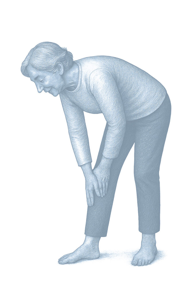 Starsza kobieta pochylona w przód wykonuje ćwiczenie skłonu, opierając dłonie na nodze.