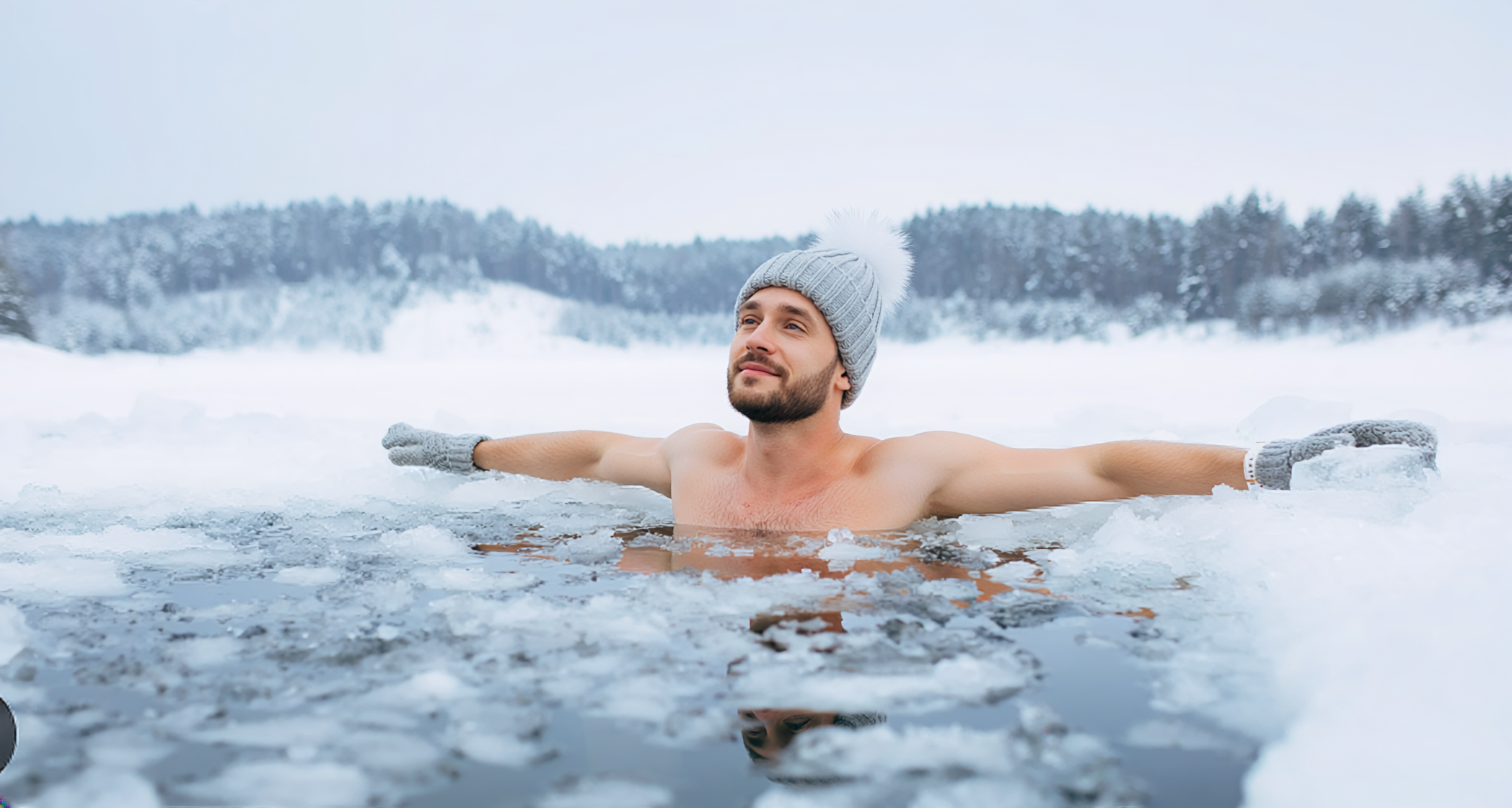 Mężczyzna zanurzony w przeręblu podczas morsowania; ma na sobie czapkę i rękawiczki, w tle zimowy, ośnieżony krajobraz.