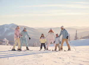 Grupa sześciu osób, w tym dorośli i dzieci, jadąca razem na nartach po zaśnieżonym stoku z malowniczymi górami w tle.