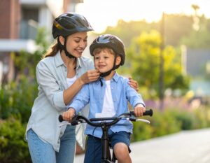 Mama zapina kask chłopcu siedzącemu na rowerze przed przejażdżką w słoneczny dzień.