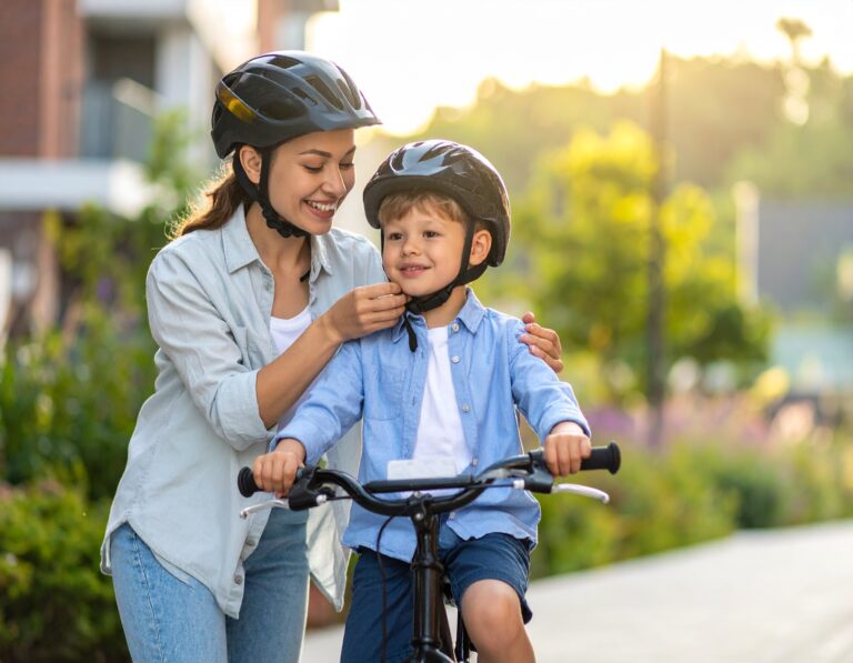 Mama zapina kask chłopcu siedzącemu na rowerze przed przejażdżką w słoneczny dzień.