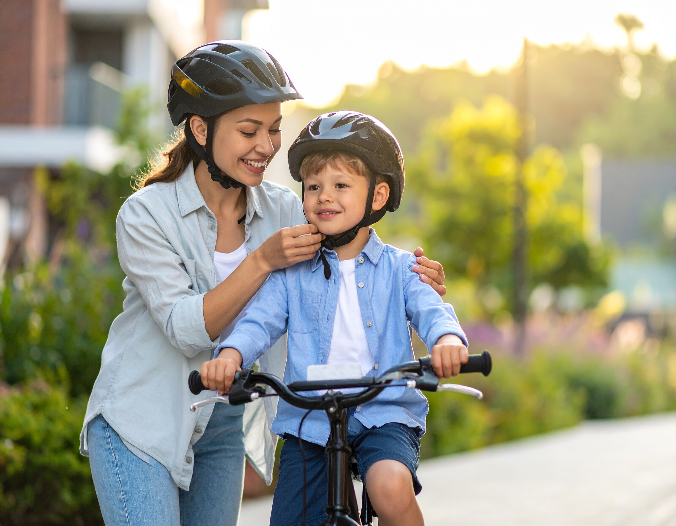 Mama zapina kask chłopcu siedzącemu na rowerze przed przejażdżką w słoneczny dzień.