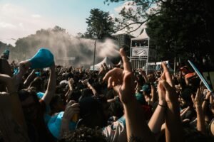 Tłum uczestników festiwalu na świeżym powietrzu, z uniesionymi rękami, podczas wydarzenia w upalny dzień i rozpylanej wodnej mgiełki chłodzącej.